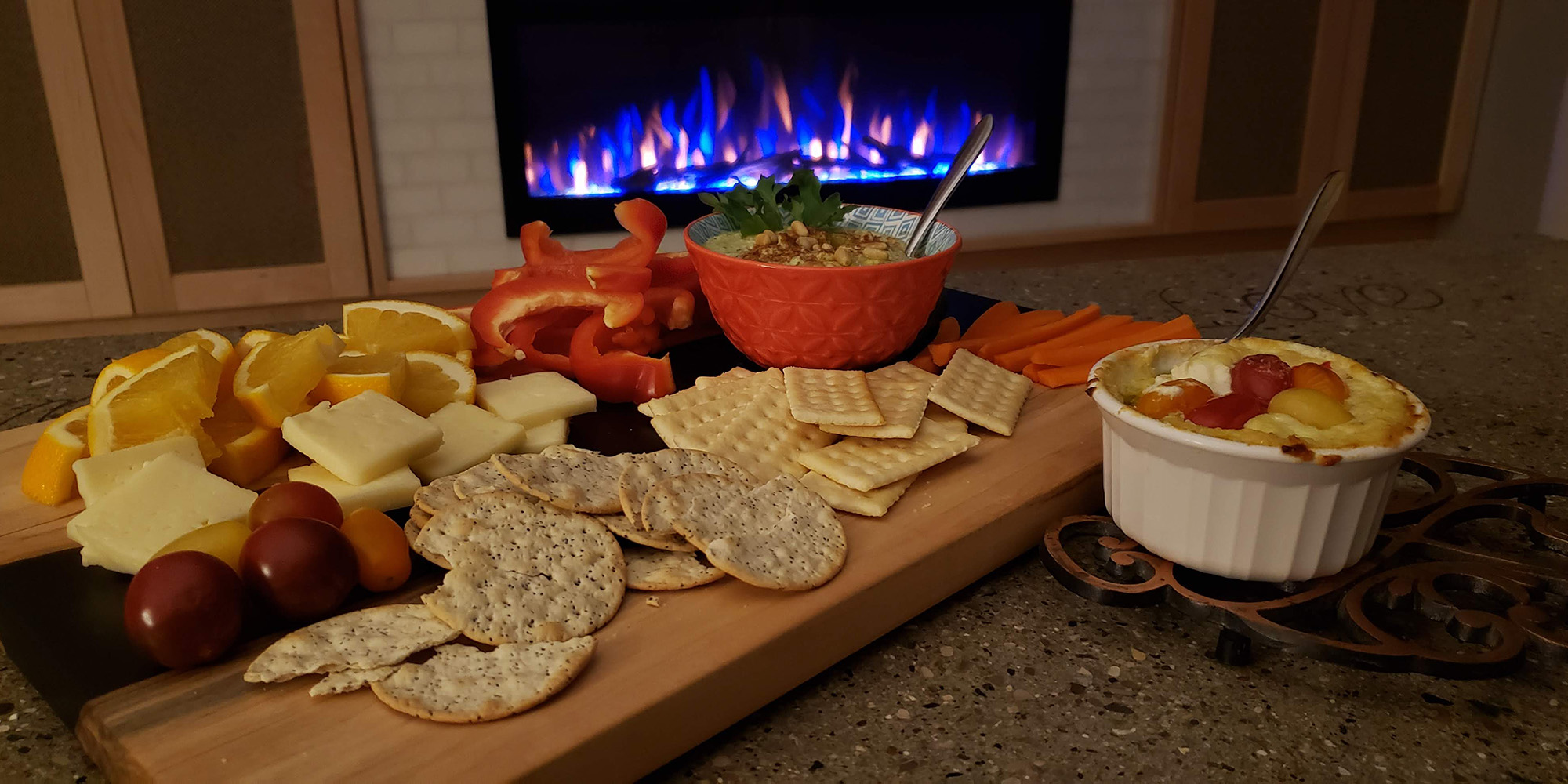 Charcuterie serving board viewed on concrete coffee table in front of fireplace in custom entertainment center